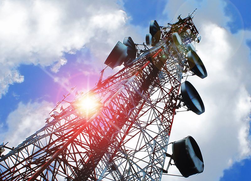 A communications tower with sector antennas against a bright sky